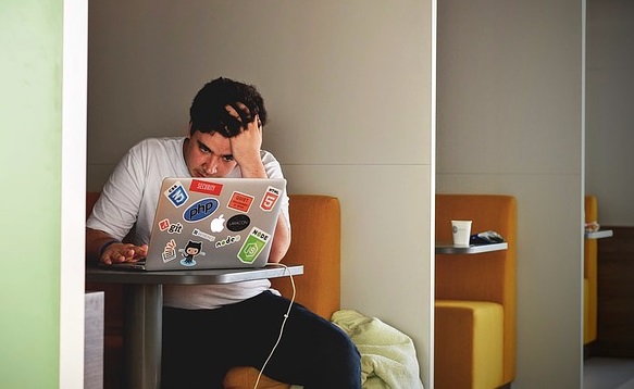 A man with his hand in his hair frustrated while working on his computer